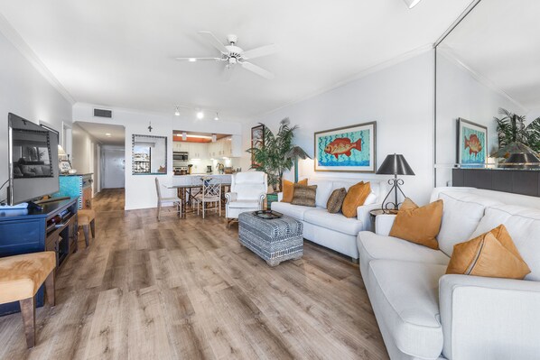 Un salon moderne avec un canapé blanc, un plancher en bois et un ventilateur de plafond.
