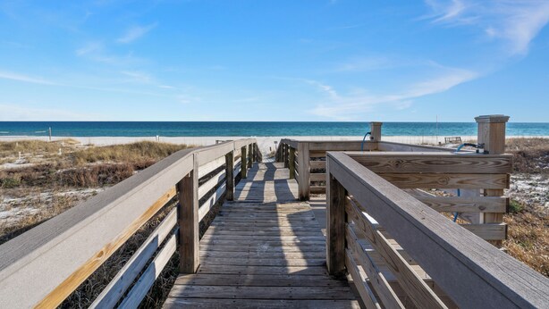 A wooden boardwalk leading to a beach with a clear blue sky.