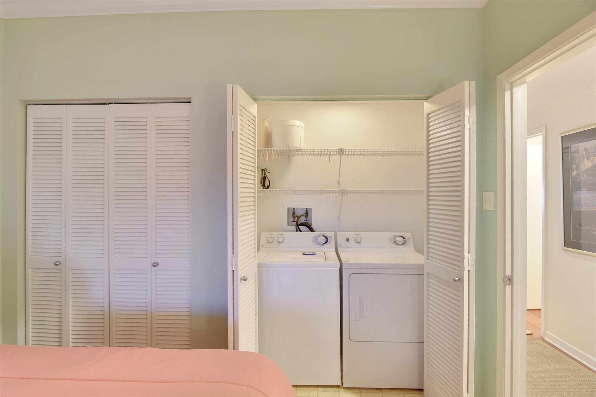A laundry room with a washing machine and dryer, a small shelf with a container, and a door with a towel rack.