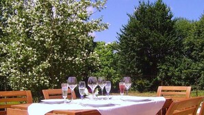 An outdoor dining table set with chairs, surrounded by greenery and trees.