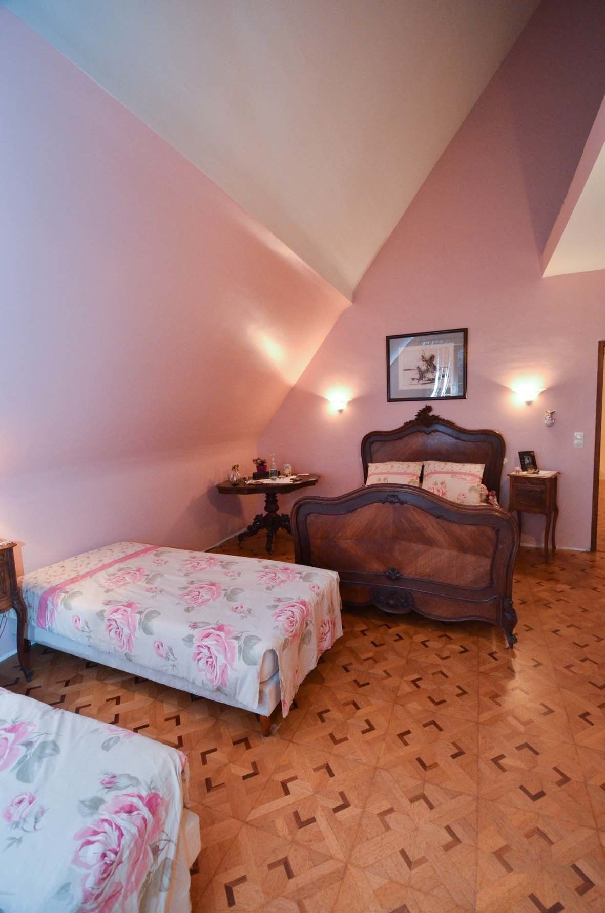 A bedroom with a large bed, a smaller bed, a nightstand, a wall-mounted picture, and a patterned floor.