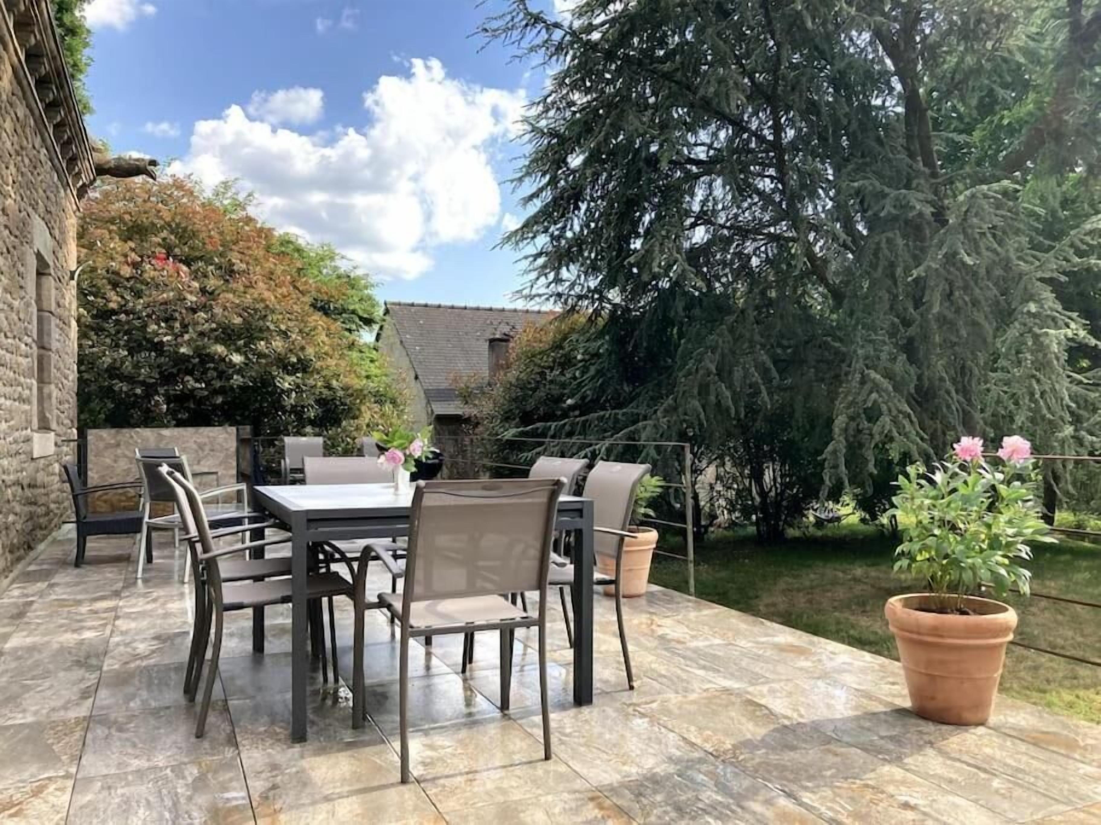 An outdoor patio with a table and chairs, surrounded by a stone floor and potted plants.