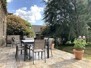 An outdoor patio with a table and chairs, surrounded by a stone floor and potted plants.
