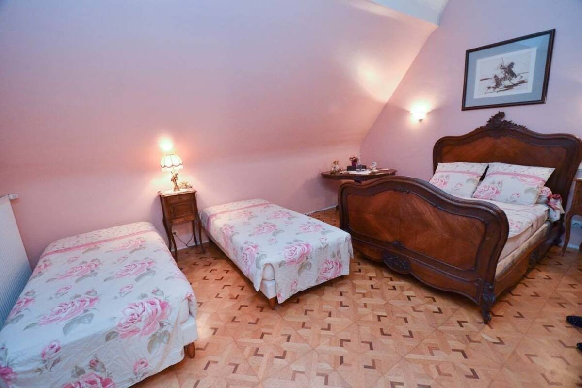 Quarto com uma cama grande, duas camas menores, uma mesa de cabeceira, um abajur e um quadro na parede.
