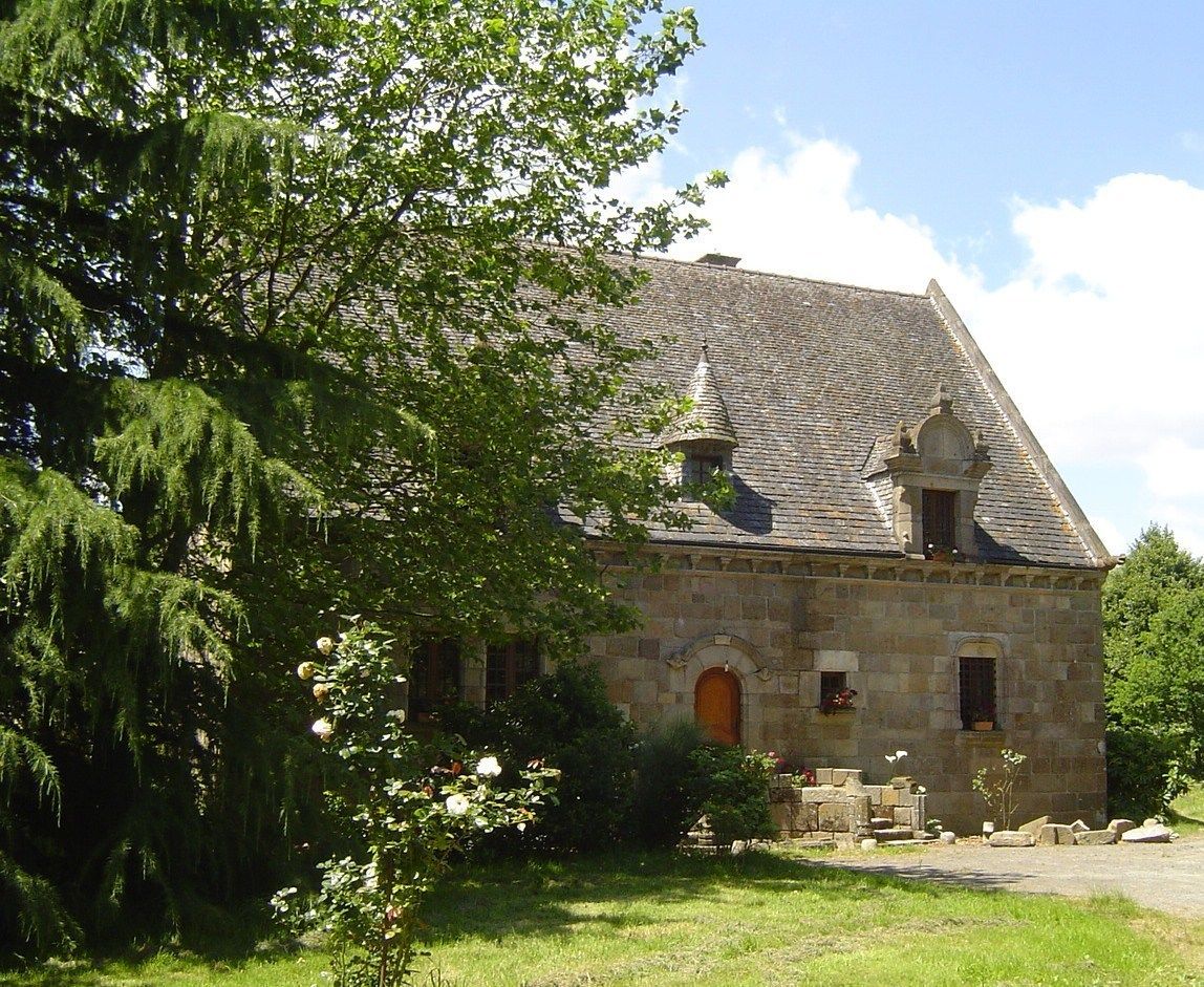 A stone building with a steeply pitched roof, a central entrance with an arch, and a small tower-like structure on the roof.