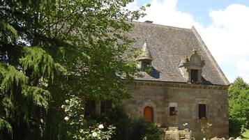 A stone building with a steeply pitched roof, a central entrance with an arch, and a small tower-like structure on the roof.