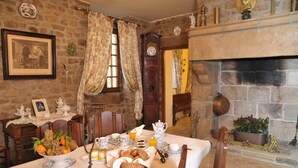 A dining room with a stone wall, a fireplace, a clock, and a table set with breakfast.