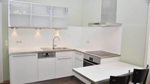 A modern kitchen with white cabinetry, a built-in dishwasher, a stove, and a dining area with a table and chairs. - Café & Hotel Daheim (Masserberg)