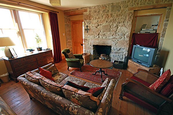 A cozy living room with a stone fireplace, a sofa, a television, and a window with curtains.