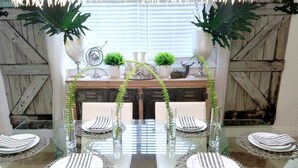 A dining table set with striped napkins, white plates, and glassware, surrounded by potted plants and decorative items.