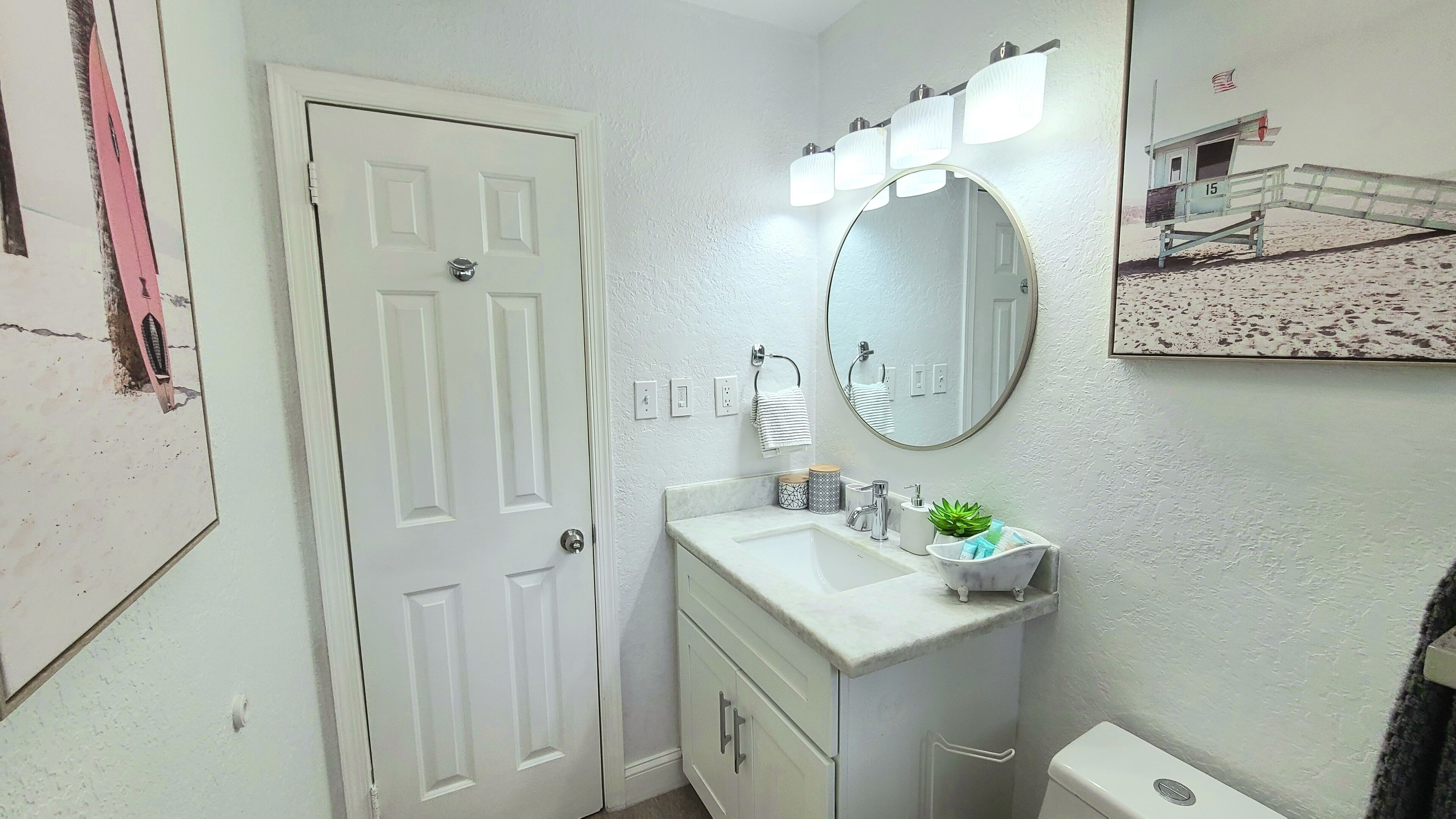 A bathroom with a white door, a sink with a mirror above it, and a toilet.