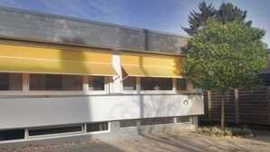 A modern building with a flat roof, large windows, and a tree in the foreground. - Haus am See B&B (Bornheim)