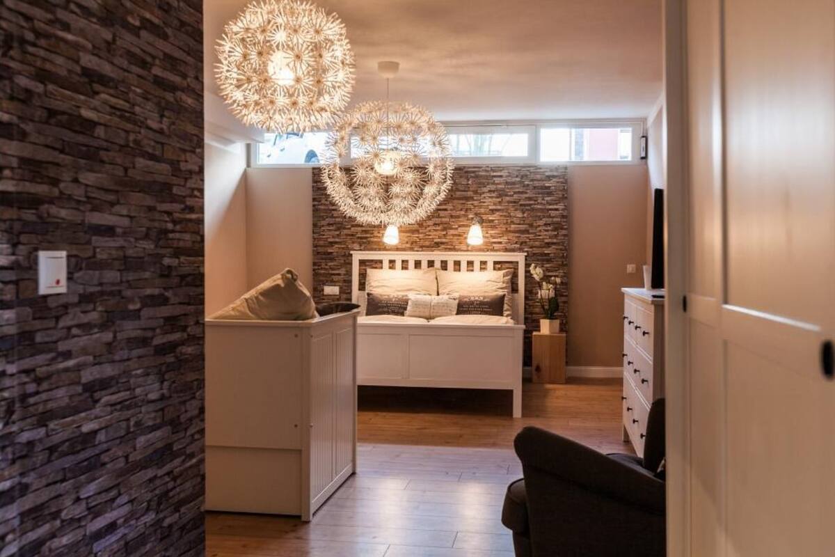 Quarto com parede de pedra, cama com peseira, mesas de cabeceira e um grande candeeiro circular.