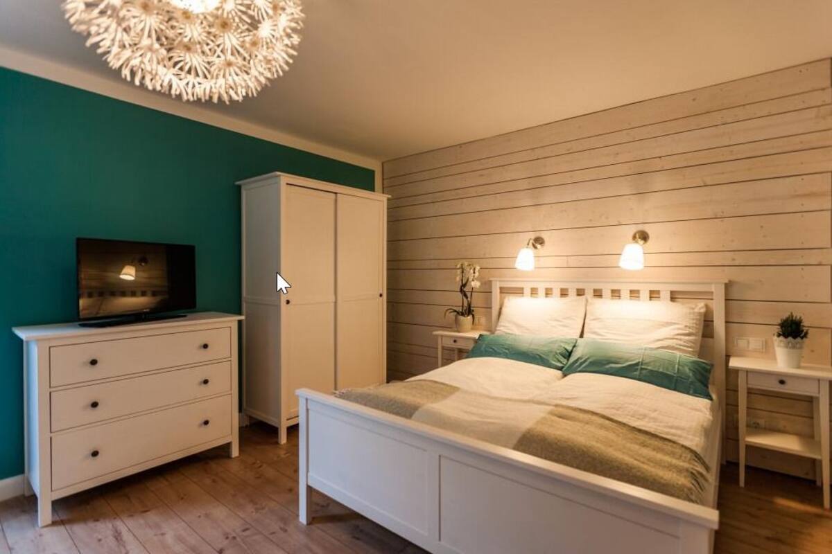 Quarto com cama, penteadeira, televisão e luminária fixada na parede.