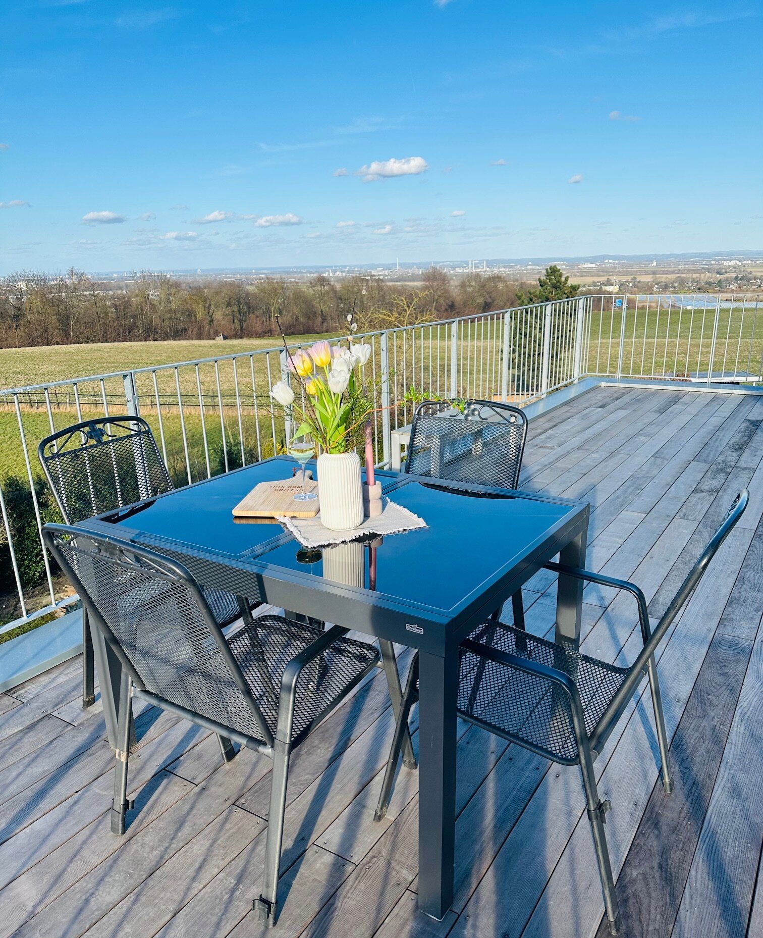Eine Terrasse im Freien mit Tisch und Stühlen, einer Blumenvase und Blick auf die Landschaft.