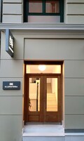 Egy épület bejárata, amelyben két szárnyú ajtó és egy lépcső vezet a belseje felé. Az ajtó felett egy tábla található, amelyen a következő felirat olvasható: „KLEPSYDRA”.