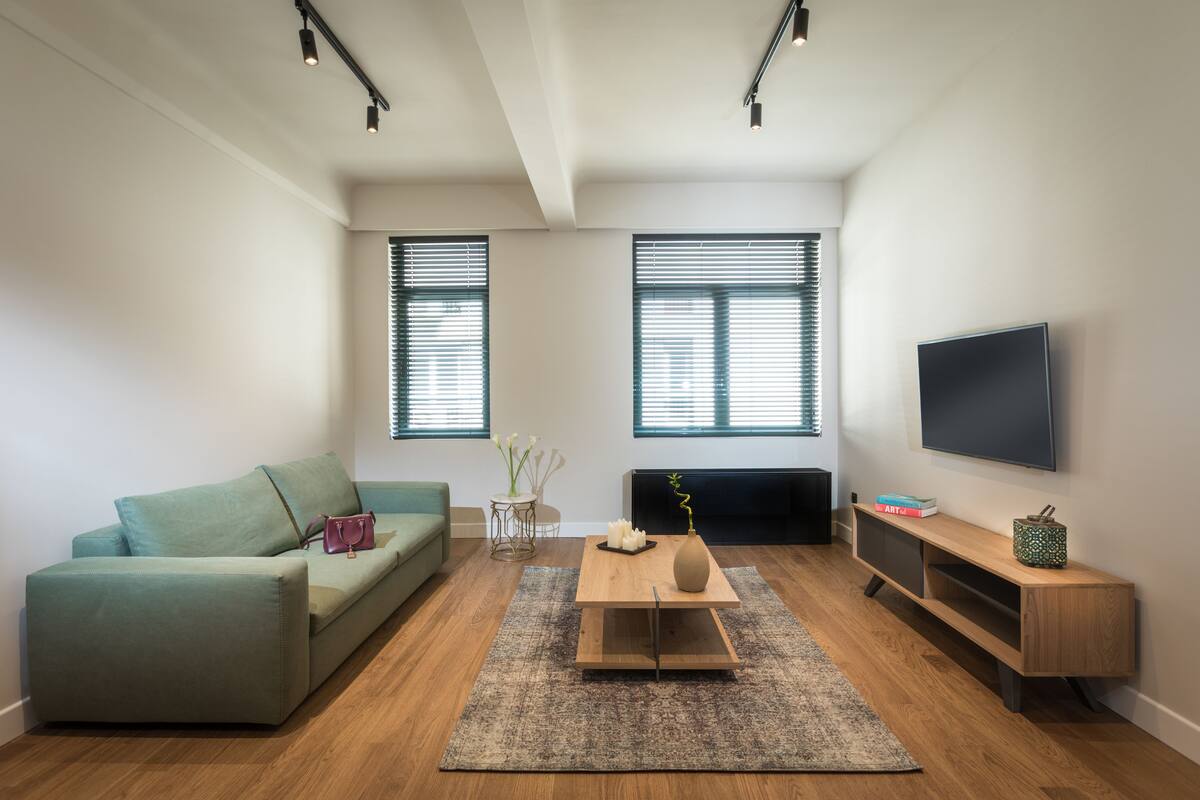 A modern living room with a green sofa, a coffee table, a TV mounted on the wall, and a fireplace.