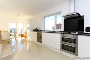 Een moderne keuken met witte kasten, een zwart aanrecht, roestvrijstalen apparatuur en een raam dat voor natuurlijk licht zorgt.