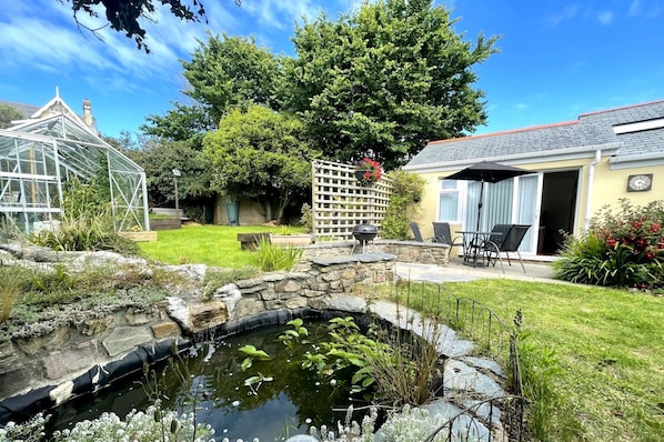 Surrounded by lush greenery, this serene outdoor space features a small pond, patio, and a greenhouse, perfect for relaxation and nature appreciation.