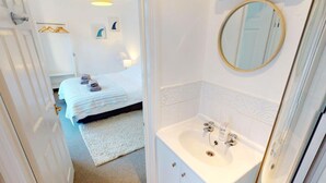 Habitación de hotel con cama, baño con lavamanos y espejo, y pasillo con puerta.