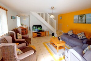A modern living room with a staircase, a television, and a dining area.