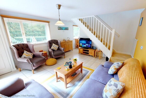 A living room with a sofa, armchair, coffee table, TV, and a staircase. - Windermere Lodge 2 Bedrooms (Windermere)