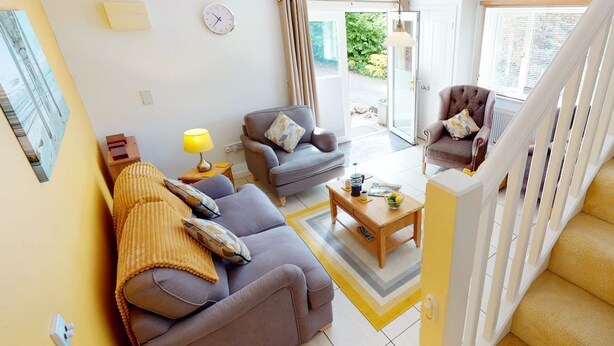 A modern living room with a sofa, armchairs, and a coffee table. There is a staircase with a railing, and a door leading outside. - Windermere Lodge 2 Bedrooms (Windermere)