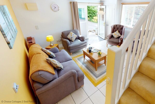 A modern living room with a sofa, armchairs, and a coffee table. There is a staircase with a railing, and a door leading outside. - Windermere Lodge 2 Bedrooms (Windermere)