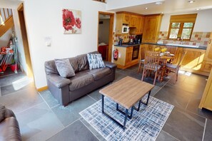 A modern kitchen with wooden cabinets, a dining area with a table and chairs, a sofa with cushions, and a painting on the wall.