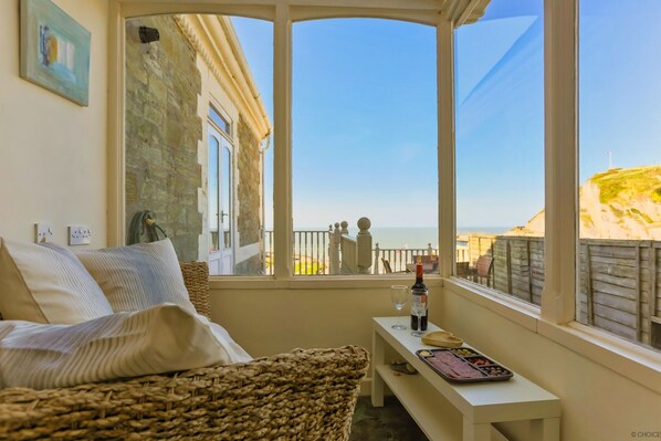 A room with a view of the sea, a bed, a bench, and a table with food and drinks.