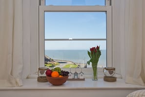 Enjoy the serene sea view from your room, featuring a bowl of fresh fruits and a vase with vibrant flowers.