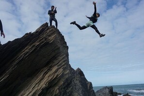 A person jumping off a rocky cliff with a body of water in the background. - Ilfracombe Raphael 2 Bedrooms (Ilfracombe)