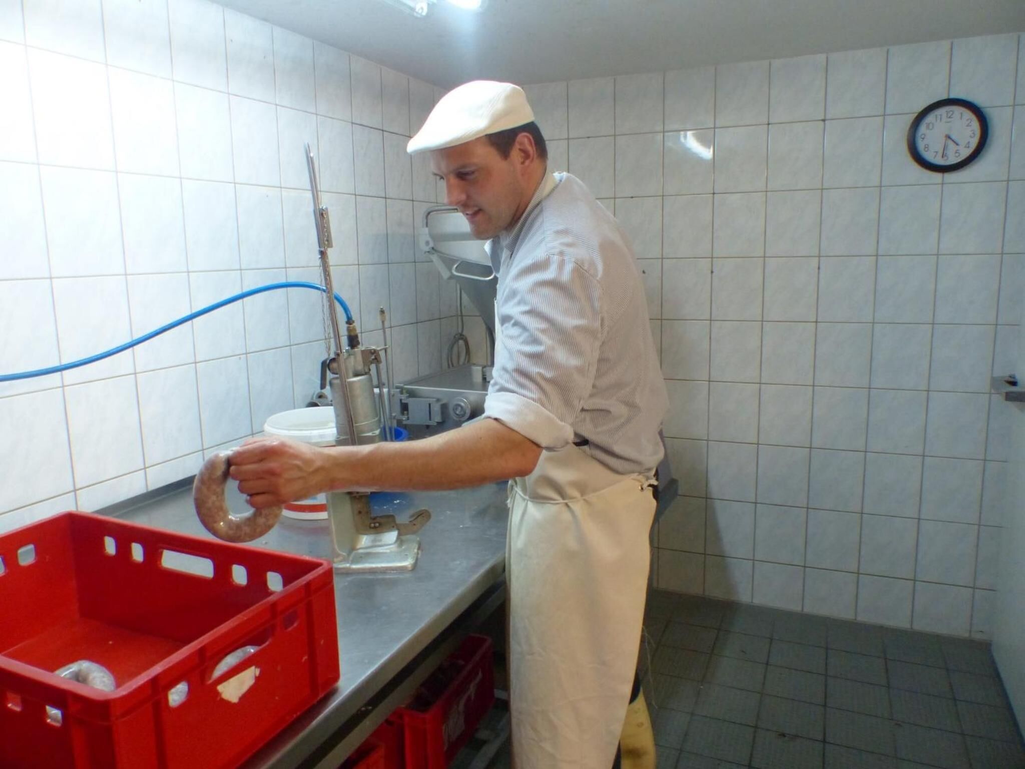 A person working in a kitchen with tiled walls, a clock, and red storage bins.