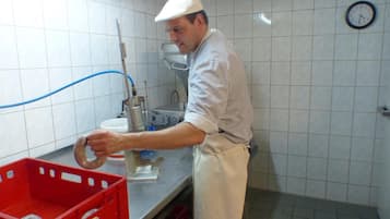 A person working in a kitchen with tiled walls, a clock, and red storage bins.