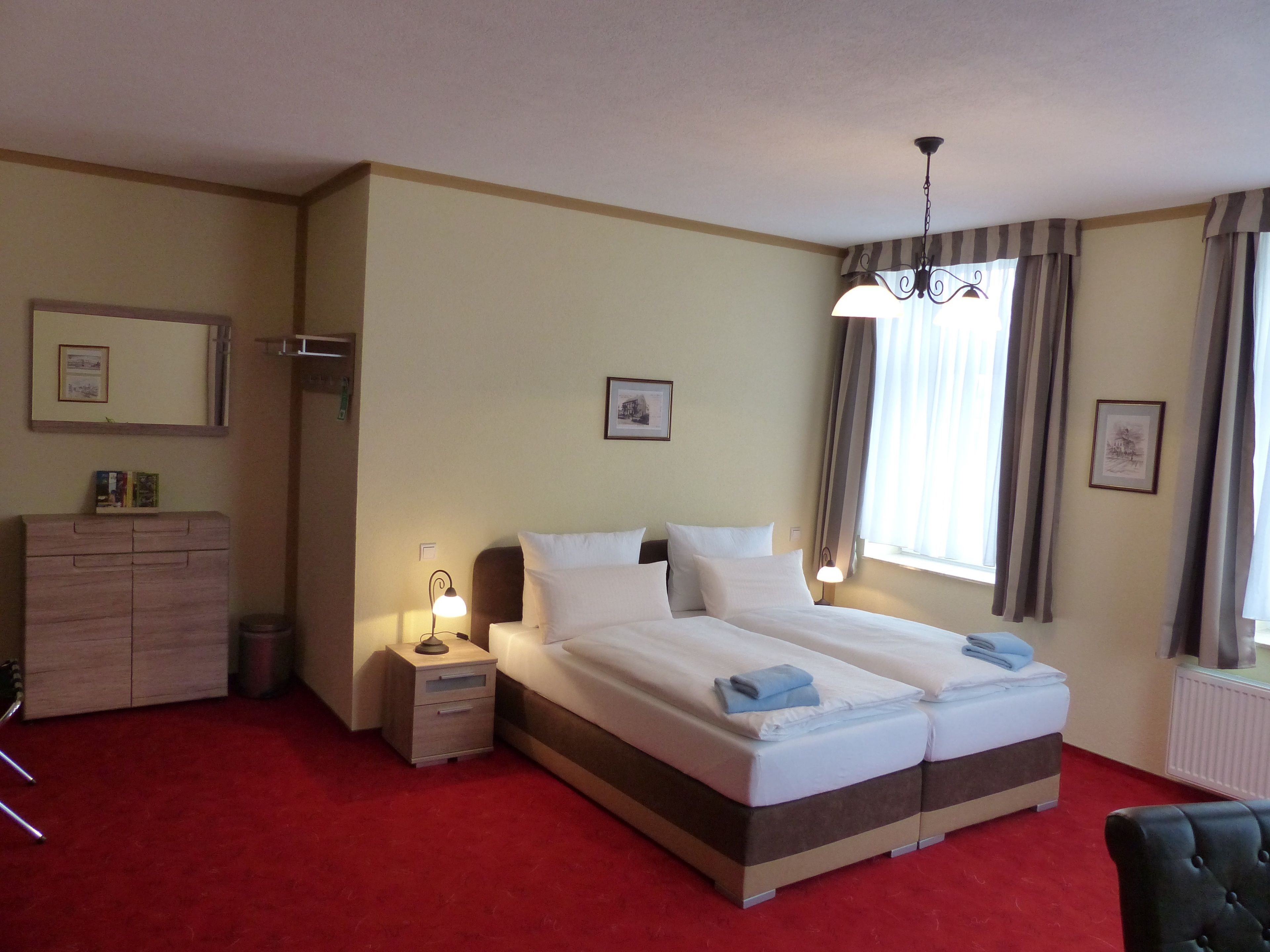 A double bed with white linens, a nightstand with a lamp, a dresser, and a chair.