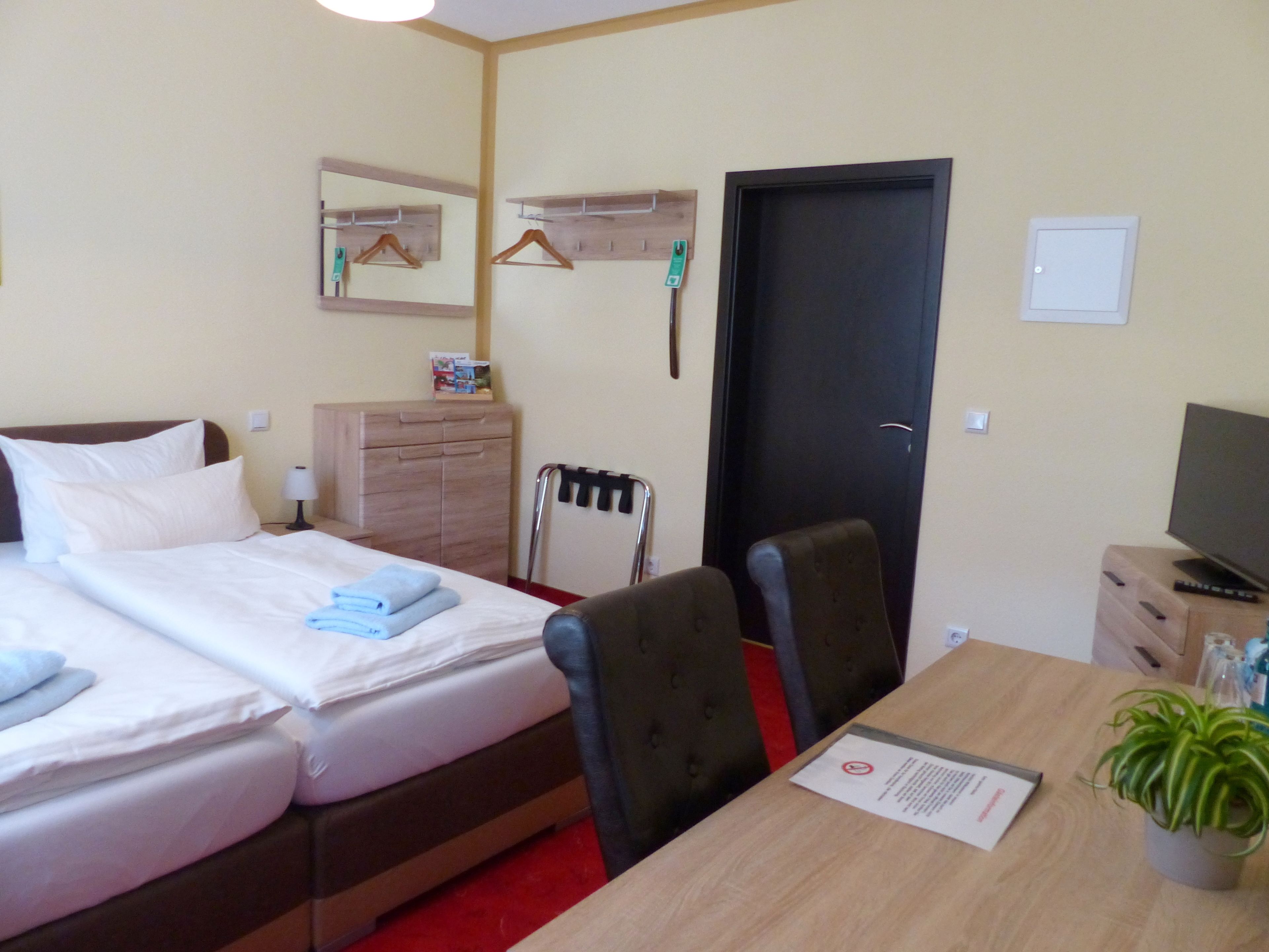 Habitación de hotel con dos camas, un escritorio, una silla, un televisor, un aparador, un espejo y una puerta.