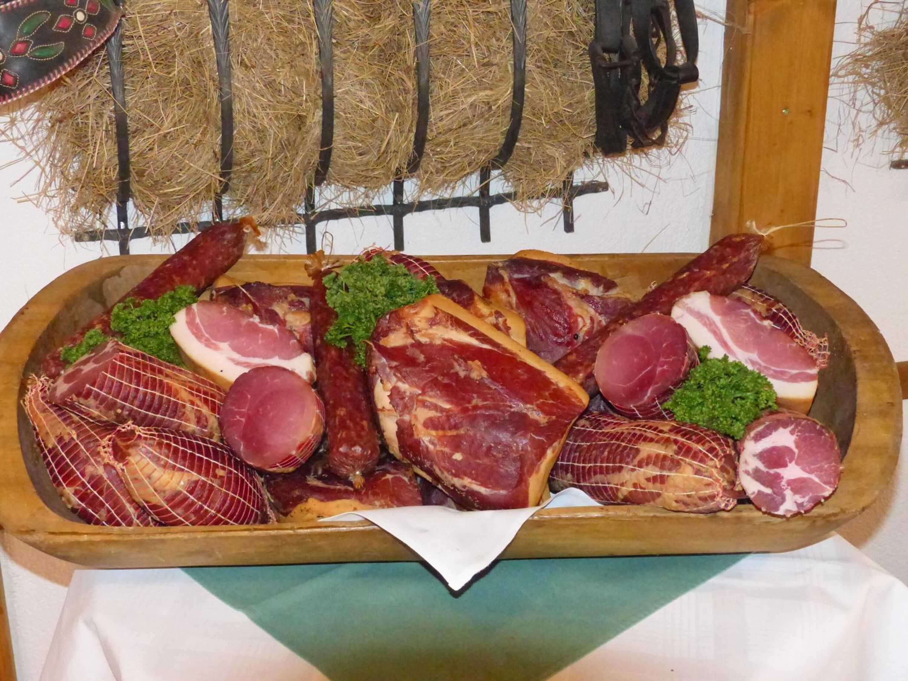 A wooden tray with various cuts of meat, including ham and bacon, garnished with parsley.