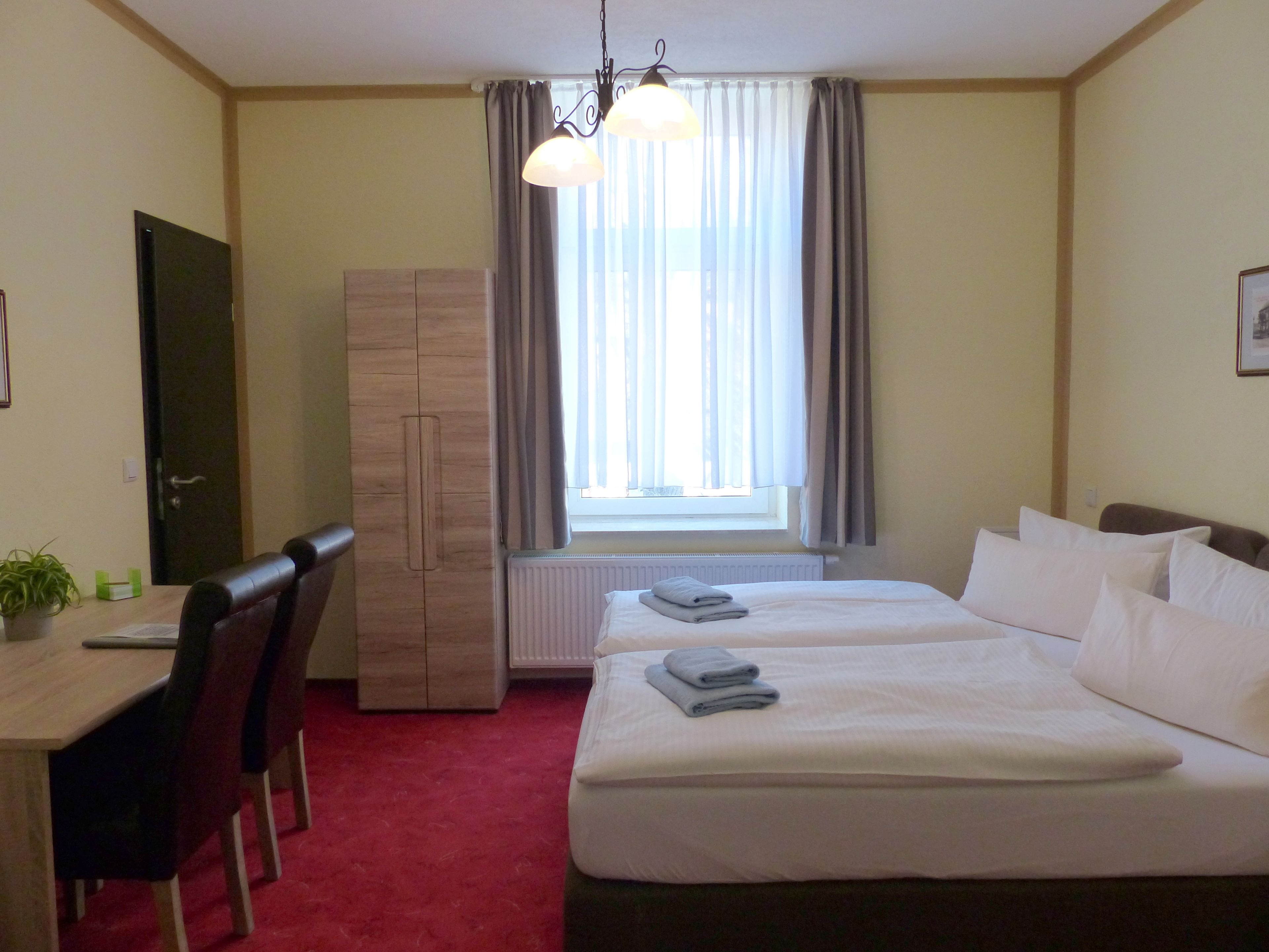 A hotel room with a bed, a desk, chairs, a wardrobe, and a window with curtains.