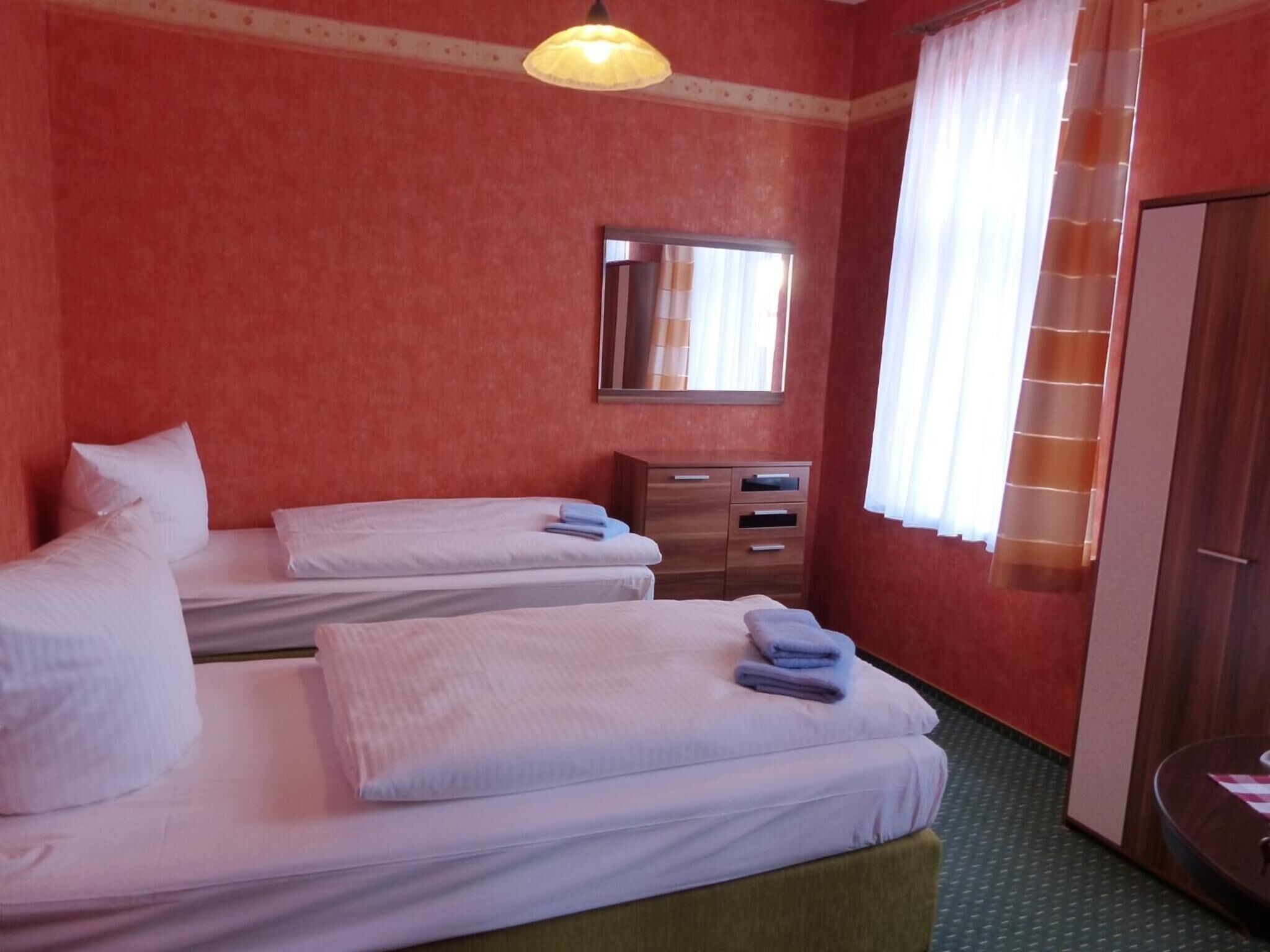 A hotel room with two beds, a wooden dresser, a mirror, and a window with curtains.