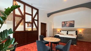 A hotel room with a bed, a round table with chairs, a large potted plant, and a brick wall. - Hotel Friedchen (Artern/Unstrut)