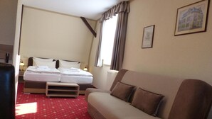 A hotel room with a bed, a sofa, a red carpet, and a window with curtains. - Hotel Friedchen (Artern/Unstrut)