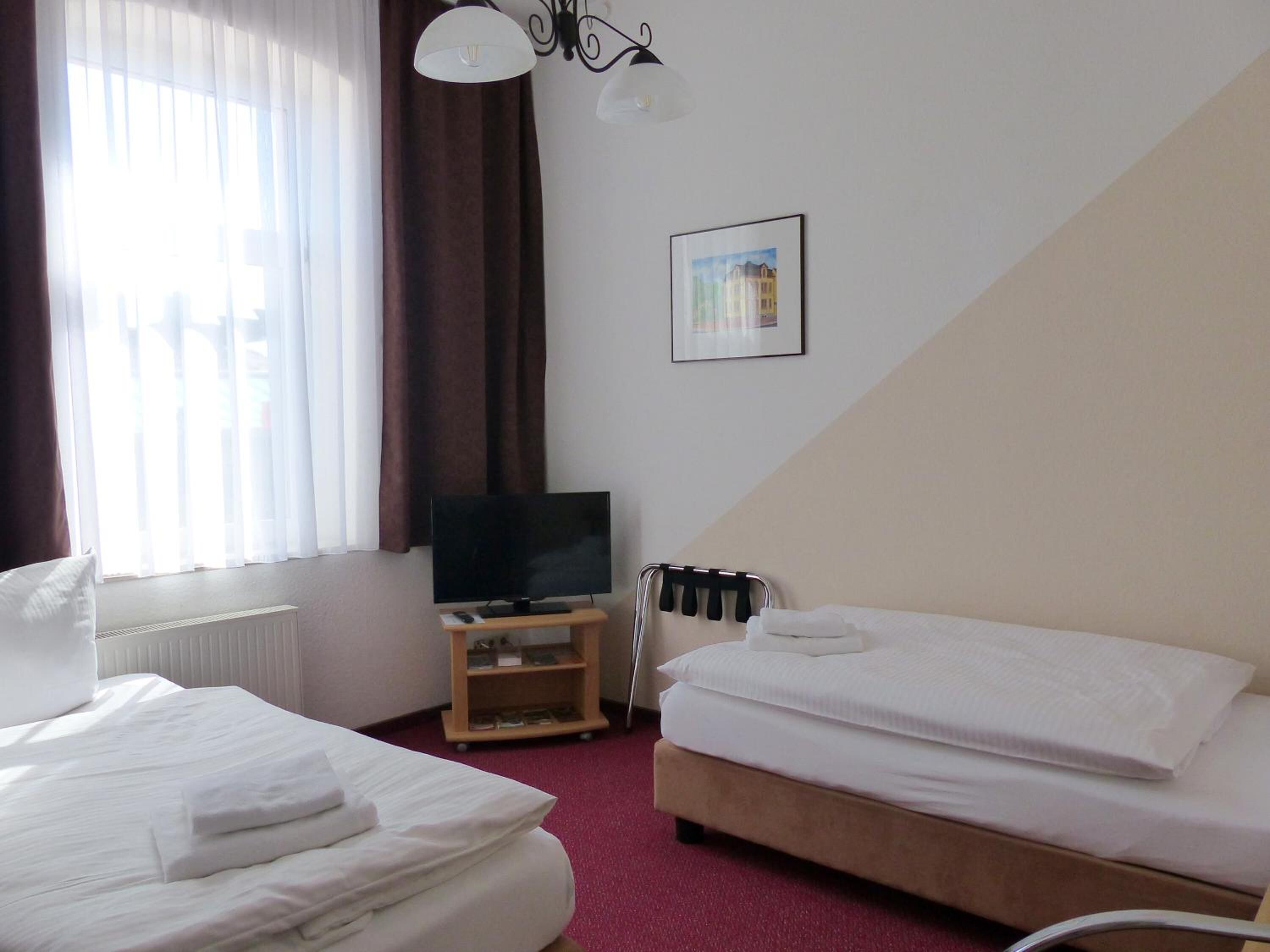 Een hotelkamer met twee bedden, een televisie, een radiator en een raam met gordijnen.