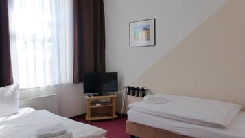Een hotelkamer met twee bedden, een televisie, een radiator en een raam met gordijnen.