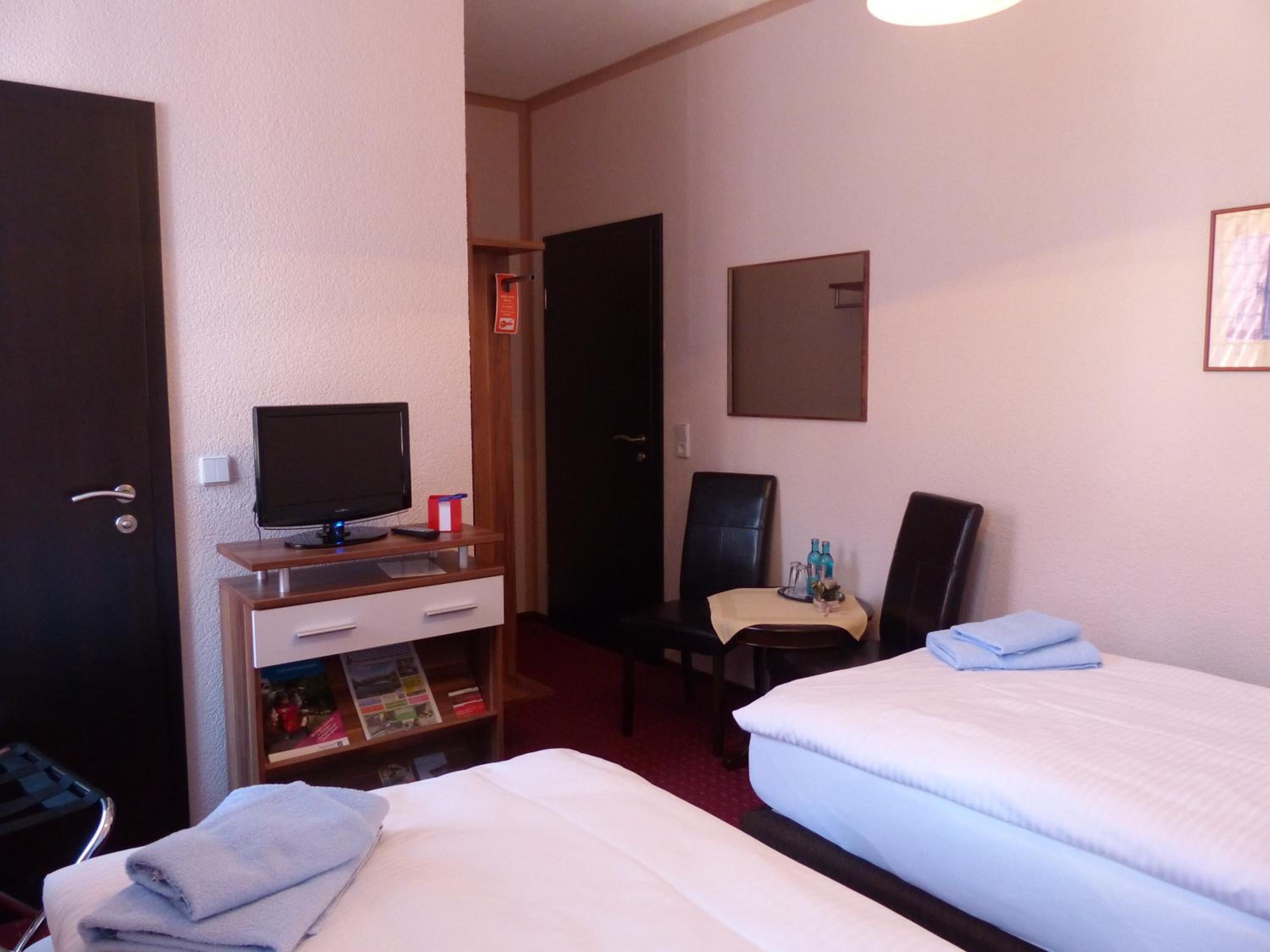 Habitación de hotel con dos camas, un escritorio con televisor, una silla y una mesita con bandeja.