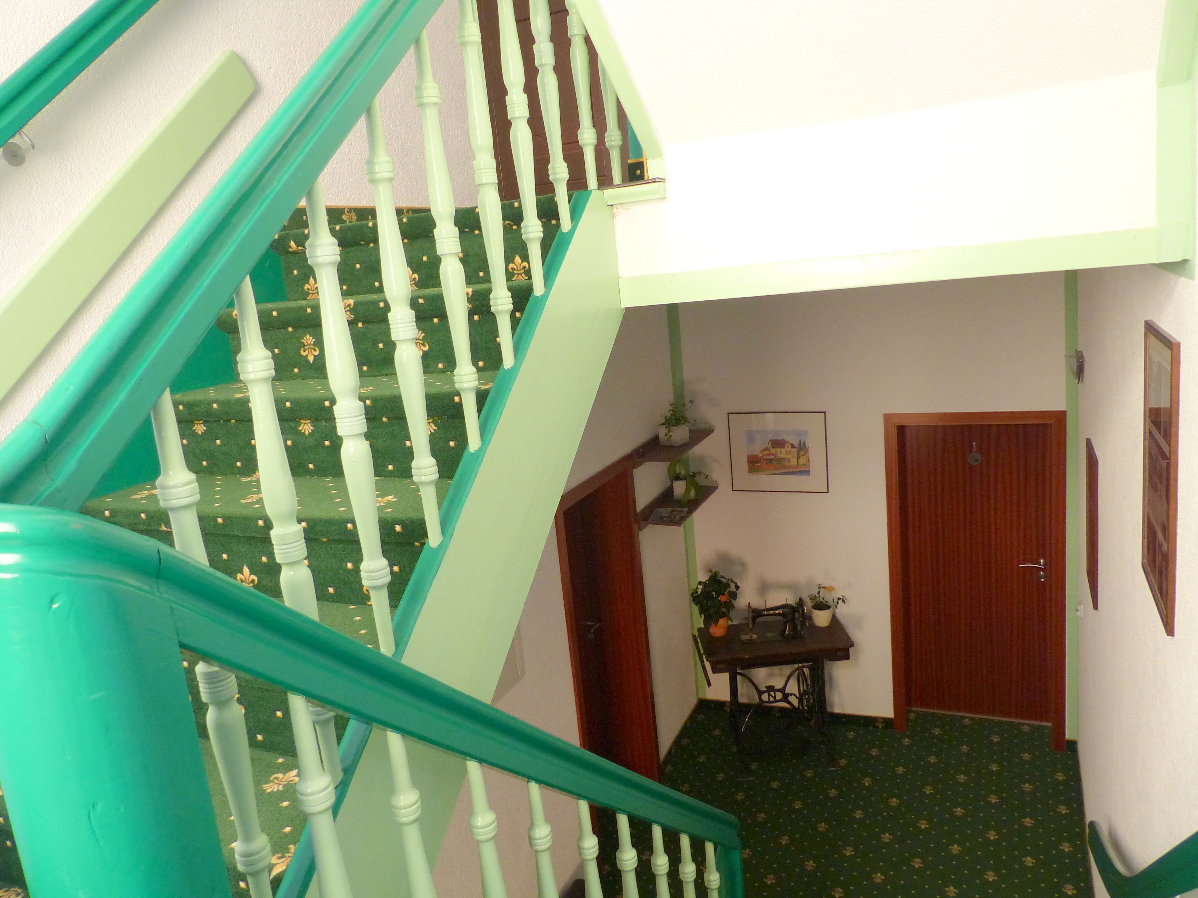 A staircase with white balusters and green handrails, leading to a room with a sewing machine, a small table, and a door.