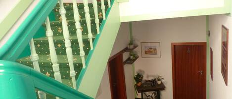 Una escalera con balaustres blancos y barandas verdes que conduce a una habitación con una máquina de coser, una pequeña mesa y una puerta.