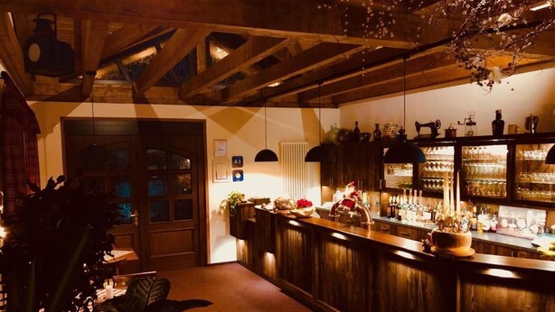 A bar area with wooden beams, a counter with various bottles, and a hanging light fixture. - Hotel Friedchen (Artern/Unstrut)