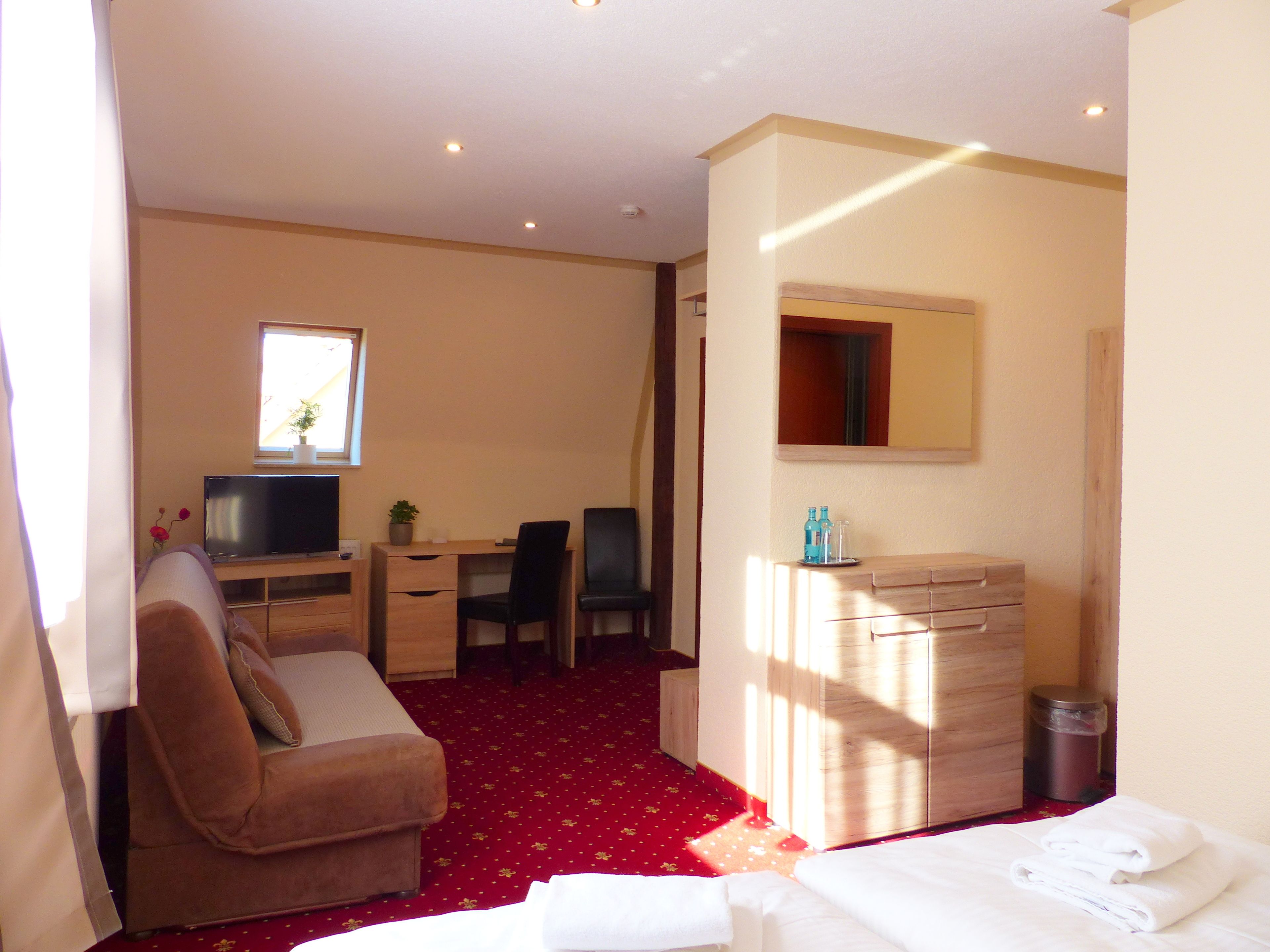 Habitación de hotel con cama, escritorio, silla, televisor, cómoda y basurero.