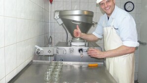 A kitchen with stainless steel appliances, a clock on the wall, and a person giving a thumbs-up. - Hotel Friedchen (Artern/Unstrut)