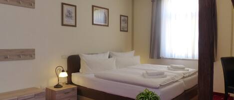 Una habitación de hotel con una cama grande, una mesita de noche con una lámpara, una pequeña mesa con una planta y una silla.